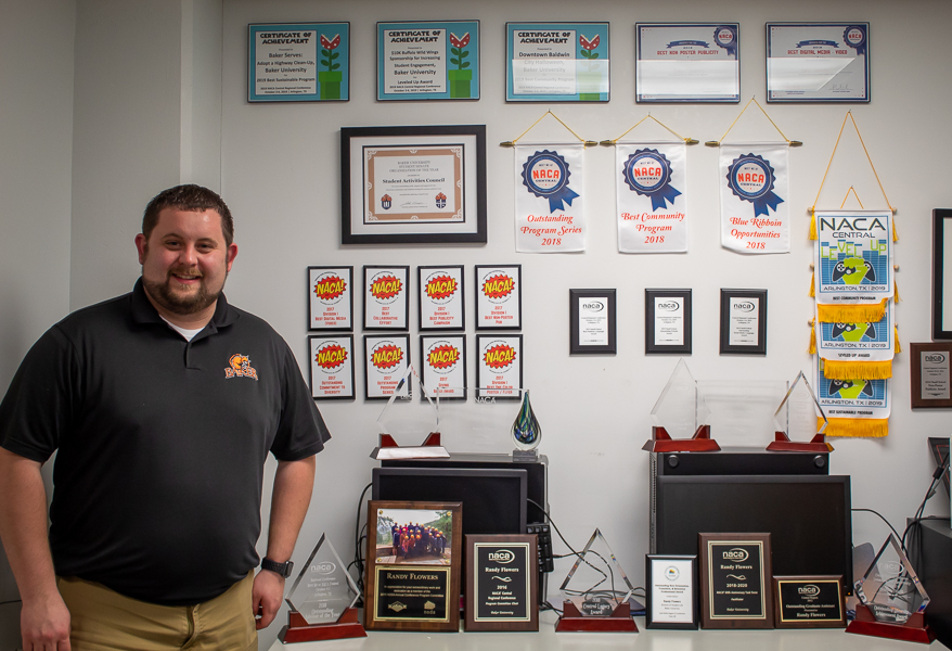 Randy Flowers standing in front of only a few of many awards he has been given during his time at Baker University. 