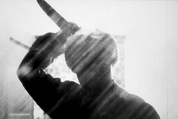 A shadow of a man stands, holding a knife above his head. Picture is in black and white.